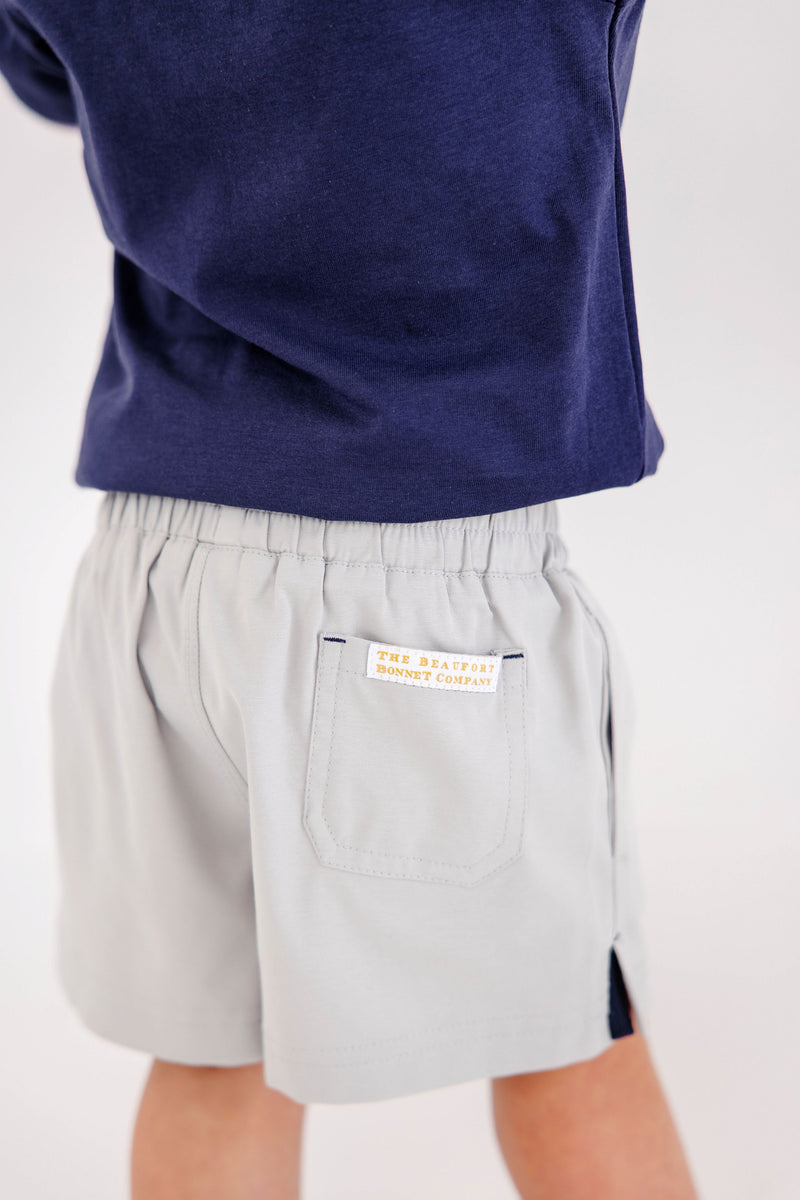 Child wearing Prepletic™ Sheffield Shorts - Grantley Gray, featuring moisture-wicking light gray fabric, an elastic waist, and a back pocket with a small brand label.