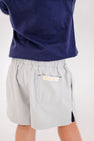 Child wearing Prepletic™ Sheffield Shorts - Grantley Gray, featuring moisture-wicking light gray fabric, an elastic waist, and a back pocket with a small brand label.