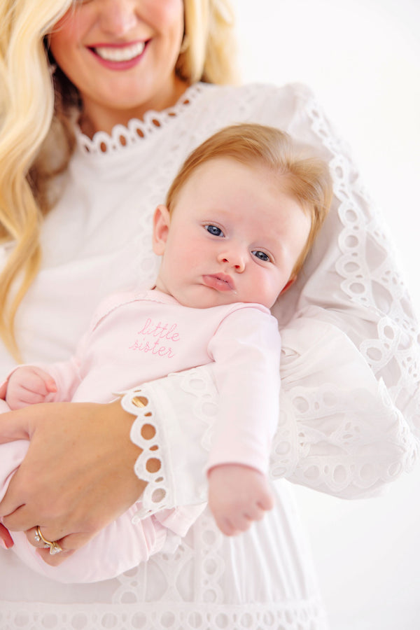 A woman in a white lace blouse holds an infant wearing a Cameron Cross Front Set - Palm Beach Pink with Hamptons Hot Pink Little Sister pima cotton outfit.