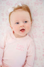 Baby wearing a Cameron Cross Front Set - Palm Beach Pink with Hamptons Hot Pink Little Sister, a light pink long-sleeve set with the words little sister embroidered on the chest.