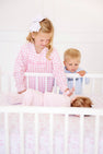 A young girl in a pink gingham sibling reveal shirt and a boy in a Cassidy Comfy Crewneck - Buckhead Blue Gingham with Nantucket Navy Big Brother look down at a baby lying in a white crib.