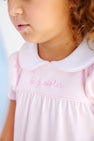 A young girl wearing the Holly Day Dress - Palm Beach Pink with Hamptons Hot Pink Big Sister, a pale pink pima cotton dress with a white rounded collar and big sister embroidered in script on the bodice.