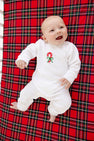 A smiling baby in The Beaufort Bonnet Company’s Paxton Playsuit – Palmetto Pearl with Candy Cane, a white velour knit holiday baby outfit, lying on a red plaid blanket.