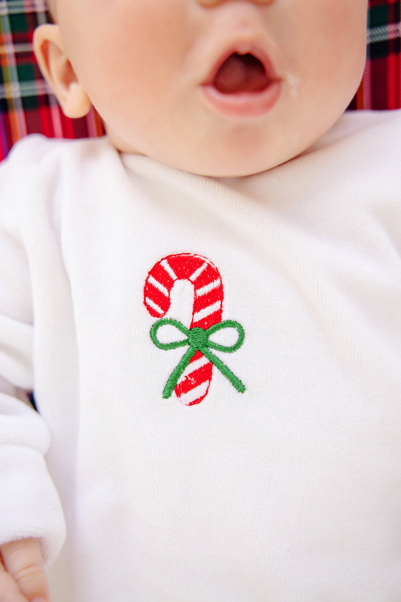 A baby dressed in The Beaufort Bonnet Company’s Paxton Playsuit – Palmetto Pearl with Candy Cane—a white velour knit holiday outfit featuring an embroidered red-and-white candy cane with a green bow; only the lower half of the baby’s face is visible, mouth open.