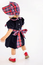A toddler models the Bellefaire Bonnet - Bucktown Tartan with Worth Avenue White Eyelet by The Beaufort Bonnet Company, paired with a velvet dress featuring a red Bucktown Tartan sash, white socks, and red shoes, standing and facing away on a white background.