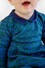 A young child wearing The Beaufort Bonnet Company’s Long Sleeve Bradford Romper in Woodlake Point Plaid with Nantucket Navy, smiling with their mouth slightly open. The image is cropped to show only the child’s lower face and upper body.