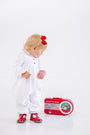 A toddler in a Long Sleeve Britt Romper - Worth Avenue White with Holly stands looking down at a vintage-style red radio on the floor.