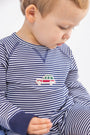 A young child in The Beaufort Bonnet Company’s Cassidy Comfy Crewneck Romper—Nantucket Navy Stripe with Wagon Embroidery—looks down, showing a side profile against a plain background.