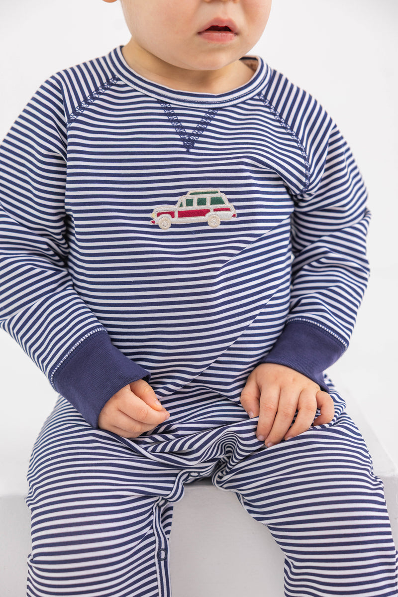 A toddler sits with hands in lap, wearing The Beaufort Bonnet Company Cassidy Comfy Crewneck Romper in Nantucket Navy Stripe with wagon embroidery on the chest.