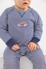 A toddler sits with hands in lap, wearing The Beaufort Bonnet Company Cassidy Comfy Crewneck Romper in Nantucket Navy Stripe with wagon embroidery on the chest.