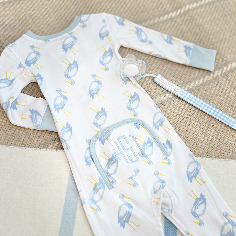 A long-sleeved blue heron print baby romper with a monogrammed front pocket, paired with a Parker Paci Clip - Blue Grand Gasparilla Gingham with Buckhead Blue on a blue and white checkered ribbon.