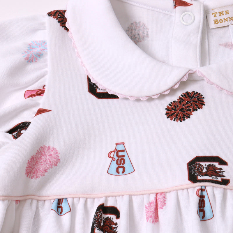 Close-up of The Beaufort Bonnet Company’s USC Britt Bubble – South Carolina Spirit with Palm Beach Pink, a white dress accented with pink trim. This soft Pima Cotton bubble features printed cheerleader pom-poms, a USC megaphone, and a rooster logo, highlighted by a scalloped collar for the perfect touch of spirited style.