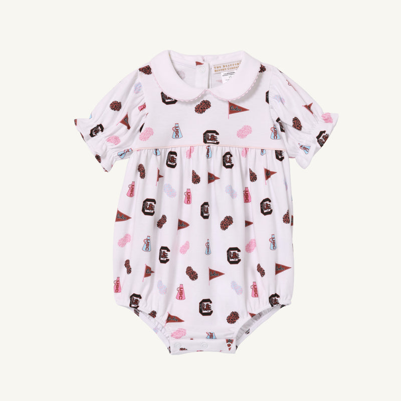 The Beaufort Bonnet Company’s USC Britt Bubble - South Carolina Spirit with Palm Beach Pink is a white baby romper with short sleeves and a Peter Pan collar, crafted from soft Pima Cotton. It features an all-over print of maroon, pink, and brown sports-related icons—including pennants, foam fingers, and megaphones—for a charming display of South Carolina Spirit.