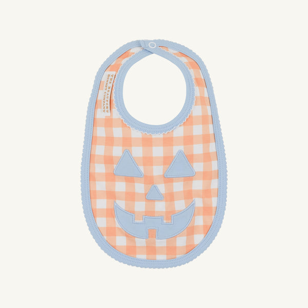 The Beaufort Bonnet Company’s Burp Me Bib - Seashore Sherbet Gingham & Beale Street Blue features an orange and white checkered pattern with light blue trim, making it a perfect fall baby essential. The front is adorned with a charming light blue jack-o-lantern face appliqué.
