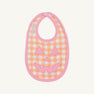 A fall baby essential, the Burp Me Bib - Seashore Sherbet Gingham & Hamptons Hot Pink by The Beaufort Bonnet Company features an orange and white gingham pattern with a hot pink trim and a cheerful pink jack-o-lantern face design on the front.