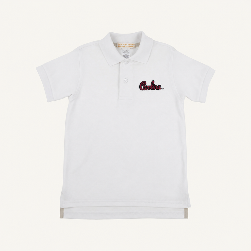 The South Carolina Prim & Proper Polo in Worth Avenue White by The Beaufort Bonnet Company is a white short-sleeve polo shirt featuring a collar, buttons, and an embroidered red South Carolina logo on the left chest. Crafted from soft Pima Cotton Knit, this polo offers a clean, classic look with its plain white background.