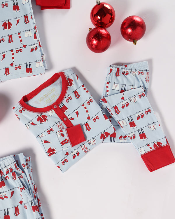 The Sutton’s Sweet Dream Set - Santa’s Laundry Line with Richmond Red from The Beaufort Bonnet Company, featuring light blue Pima cotton pajamas with red trim and a festive holiday print, is folded on a white surface beside three shiny red Christmas ornaments.