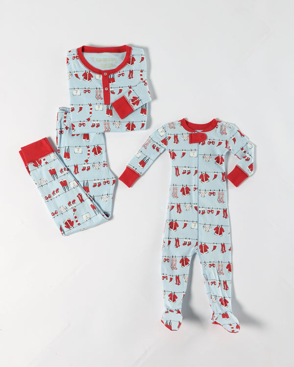 Two sets of Knox’s Night Night - Santa’s Laundry Line pajamas by The Beaufort Bonnet Company are laid flat on a white background. Made from soft Pima cotton, one set is an adult-sized two-piece with a shirt and pants featuring a whimsical winter clothes pattern and red trim, while the other is a matching one-piece designed for children or babies—perfect for coordinating family holiday pajamas.