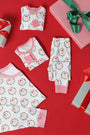 Folded and laid-out Knox’s Night Night - North Pole Portrait with Richmond Red Stripe pajamas by The Beaufort Bonnet Company are displayed on a red background, surrounded by wrapped gifts with green and red ribbons.