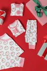 Folded and laid-out Knox’s Night Night - North Pole Portrait with Richmond Red Stripe pajamas by The Beaufort Bonnet Company are displayed on a red background, surrounded by wrapped gifts with green and red ribbons.