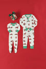 Two Sutton’s Sweet Dream Sets in The Beaufort Bonnet Company’s Serious Santa Business print—one footed and one not—are laid out on a red background next to a gift wrapped with a green ribbon.