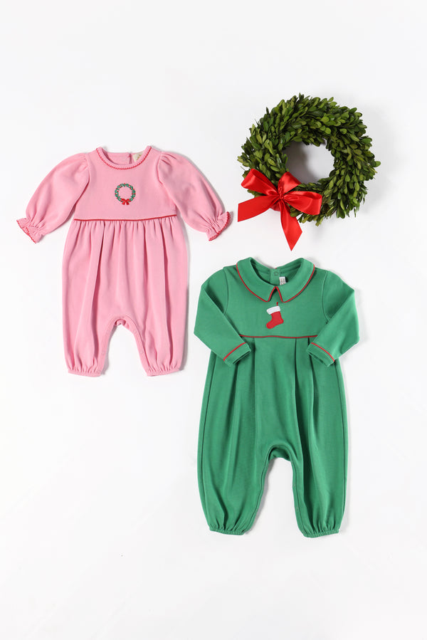 The Beaufort Bonnet Company’s Long Sleeve Ramona Ruffle Romper in Hamptons Hot Pink with Wreath Embroidery, made from soft Pima Cotton, is arranged alongside a green holiday wreath with a red bow on a white background—making the perfect festive outfit for your little one.