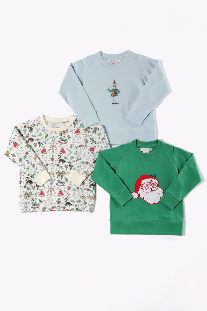 Three children’s sweatshirts from The Beaufort Bonnet Company are laid flat on a white background: one pale blue “Cassidy Comfy Crewneck - 12 Days of Christmas” featuring a nutcracker graphic, one green quilted crewneck with a Santa face, and one cream holiday party top with a colorful holiday-themed pattern.