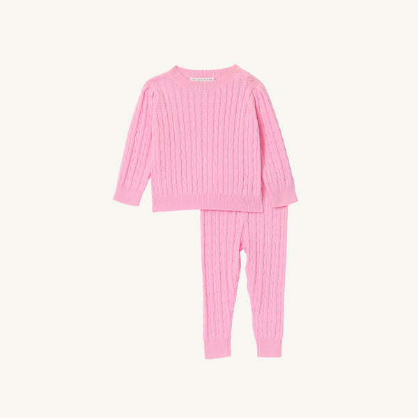 The Beaufort Bonnet Company Crawford Cable Knit Set in Pier Party Pink is a two-piece set for girls, featuring a long-sleeve sweater and matching pants with a classic cable knit pattern, displayed on a white background.