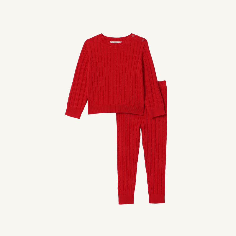 The Beaufort Bonnet Company Crawford Cable Knit Set in Richmond Red for children, featuring a long-sleeve knit sweater with button details on one shoulder and matching pants, both adorned with a classic cable pattern, laid flat against a plain white background. Made from 100% cotton to ensure comfort and quality.