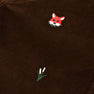 A close-up of The Beaufort Bonnet Company’s Critter Sheffield Pants in Chelsea Chocolate Corduroy, featuring a small embroidered red fox head and a tuft of green grass with two white tips.