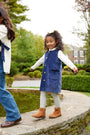 A young girl in a blue corduroy Juliet Jumper and gray Jefferies Cable Tights - Gray Heather walks along a stone ledge near a garden pond.