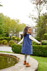 A young girl in a blue Juliet Jumper and gray Jefferies Cable Tights - Gray Heather standing by a stone garden pond.