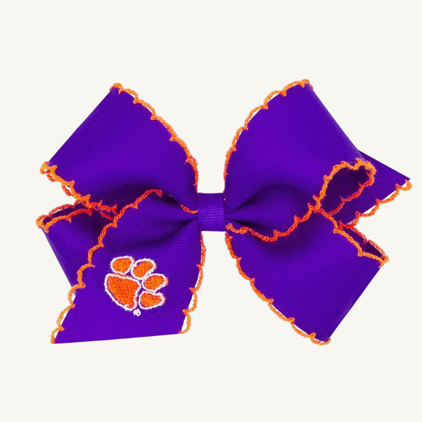 The Beaufort Bonnet Company’s Wee Ones Hair Bow - Clemson University features a purple ribbon bow with orange trim and an orange paw print emblem stitched on one loop. Set against a plain, light background, this collegiate accessory is perfect for Game Day.
