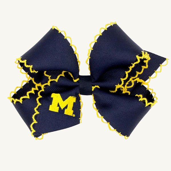 Show your Wolverines pride with the Wee Ones Hair Bow - University of Michigan by The Beaufort Bonnet Company. This navy blue hair bow features yellow zigzag trim and a yellow stitched letter M on one side, displayed against a plain white background. Perfect for any Michigan fan!.