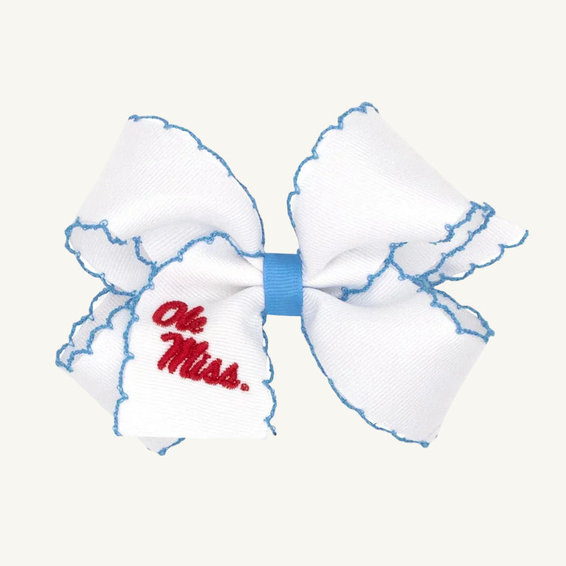 The Wee Ones Hair Bow - Ole Miss by The Beaufort Bonnet Company is a white hair bow with blue edge stitching and “Ole Miss.” embroidered in red on one side, finished with a blue center ribbon. Ideal for Game Day, it includes a no-slip hair clip to keep it securely in place.