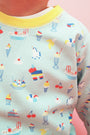 A child wearing The Beaufort Bonnet Company’s Cassidy Comfy Crewneck in Ice Cream Daydream (Blueberry Blue), a premium shirt adorned with colorful prints of sundaes, ice cream, cherries, bananas, unicorns, and piñatas. Featuring a yellow collar, this crewneck makes an excellent layering piece.