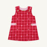 The Beaufort Bonnet Company’s Janie Jumper in Torrington Tartan with Pier Party Pink is a girls’ flannel dress for toddlers, featuring a sleeveless red tartan design, accented with small white bows, pink side bands, and gold buttons on the shoulders and waist. The dress is shown against a plain white background.