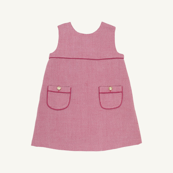 The Beaufort Bonnet Company’s Jill Jumper in Begley Berry Tweed is a sleeveless pink girls’ dress featuring two front pockets, each accented with a button and finished with dark pink trim. The classic, simple design is shown against a plain white background.
