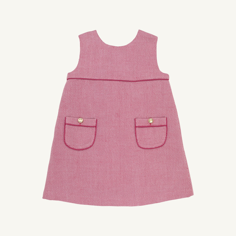 The Beaufort Bonnet Company’s Jill Jumper in Begley Berry Tweed is a sleeveless pink girls’ dress featuring two front pockets, each accented with a button and finished with dark pink trim. The classic, simple design is shown against a plain white background.