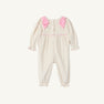 The Long Sleeve Ryleigh Romper by The Beaufort Bonnet Company features cream-colored Palmetto Pearl & Richmond Red microdot corduroy, long sleeves, delicate pink bows on the shoulders, pink piping across the chest, and ruffled cuffs at both the wrists and ankles. This charming winter outfit is displayed flat on a white background.