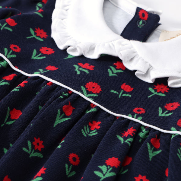 Navy blue long-sleeved Maude’s Ruffle Romper in Prescott Farms Flowers with Worth Avenue White, featuring a white ruffled Peter Pan collar and a red print.