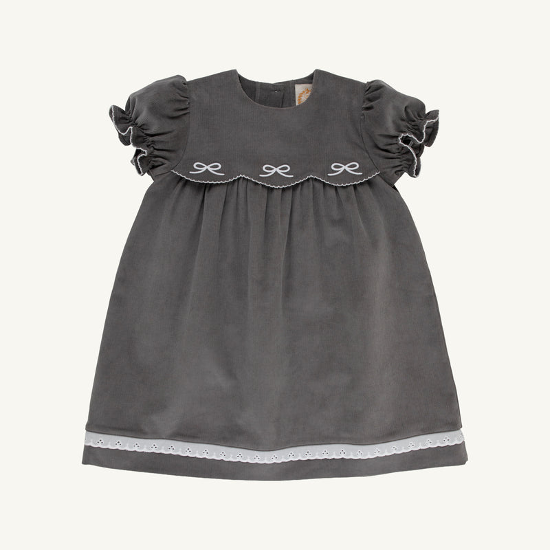 The Beaufort Bonnet Company’s McFarland Frock in Grantley Gray Corduroy with Worth Avenue White features short ruffled sleeves, a scalloped yoke adorned with embroidered bows, and a white lace trim at the hem. Displayed on a plain white background, this charming fall dress for girls adds classic style to any wardrobe.