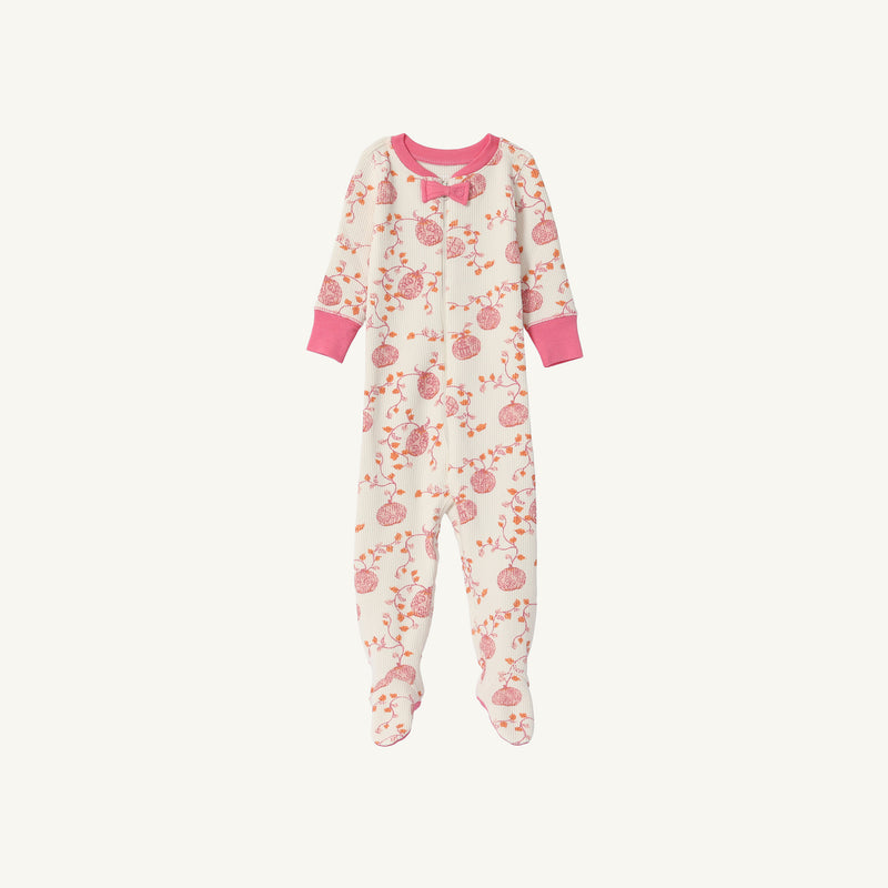Noelle’s Night Night - Gourd-geous (Palmetto Pearl) with Palm Beach Pink from The Beaufort Bonnet Company is a cozy baby sleeper featuring long sleeves, footed legs, pink cuffs, and a charming floral print adorned with pink and red flowers and fruits. A small pink bow decorates the neckline. The sleepwear is displayed on a white background.