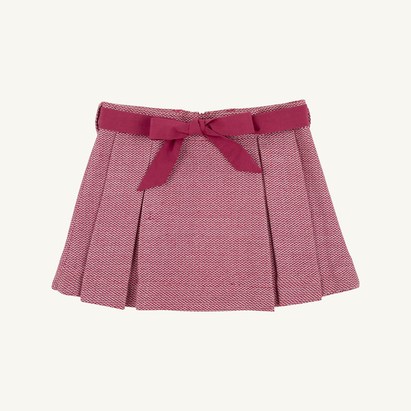 The Parson Pleated Skirt in Begley Berry Tweed by The Beaufort Bonnet Company features a pink textured pattern with elegant pleats and a coordinating pink waistband tied in a bow at the front. Shown against a plain white background, it’s the perfect fall skirt for girls.