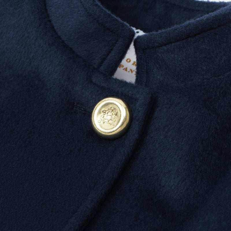 Detailed view of The Beaufort Bonnet Company’s Penelope Peacoat - Nantucket Navy for girls, highlighting the gold button adorned with a lion emblem near the collar and a glimpse of a white clothing tag beneath.