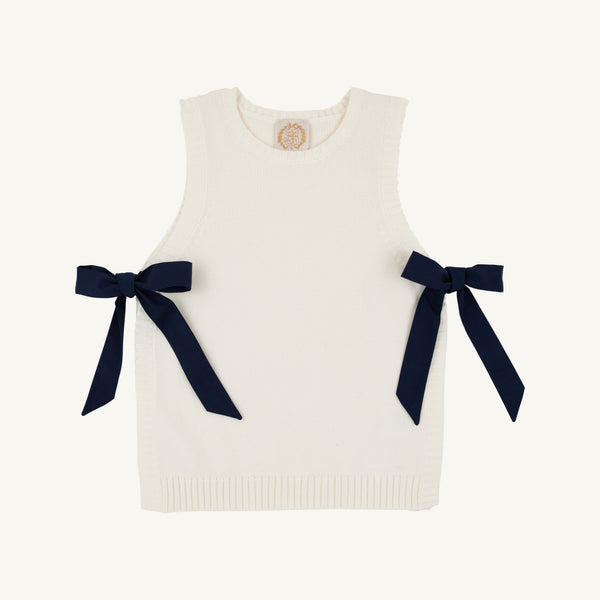 The Beaufort Bonnet Company’s Shae Sweater Vest in Palmetto Pearl with Nantucket Navy features ribbed edges and two large navy blue bows on each side, crafted from 100% cotton. Laid flat against a plain, light background, this sleeveless vest is the perfect addition to any girl’s autumn wardrobe.