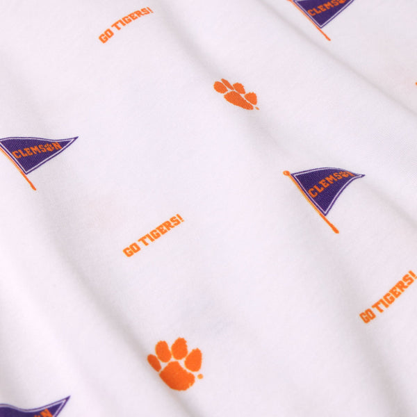 Crafted from soft Pima Cotton, the Clemson Short Sleeve Patton Play Bubble – Tiger Triumph with Clemson Orange by The Beaufort Bonnet Company features a white fabric decorated with repeating orange paw prints, purple flags labeled “Clemson,” and the phrase “Go Tigers!” in vibrant orange text—perfect for showcasing Clemson University spirit.