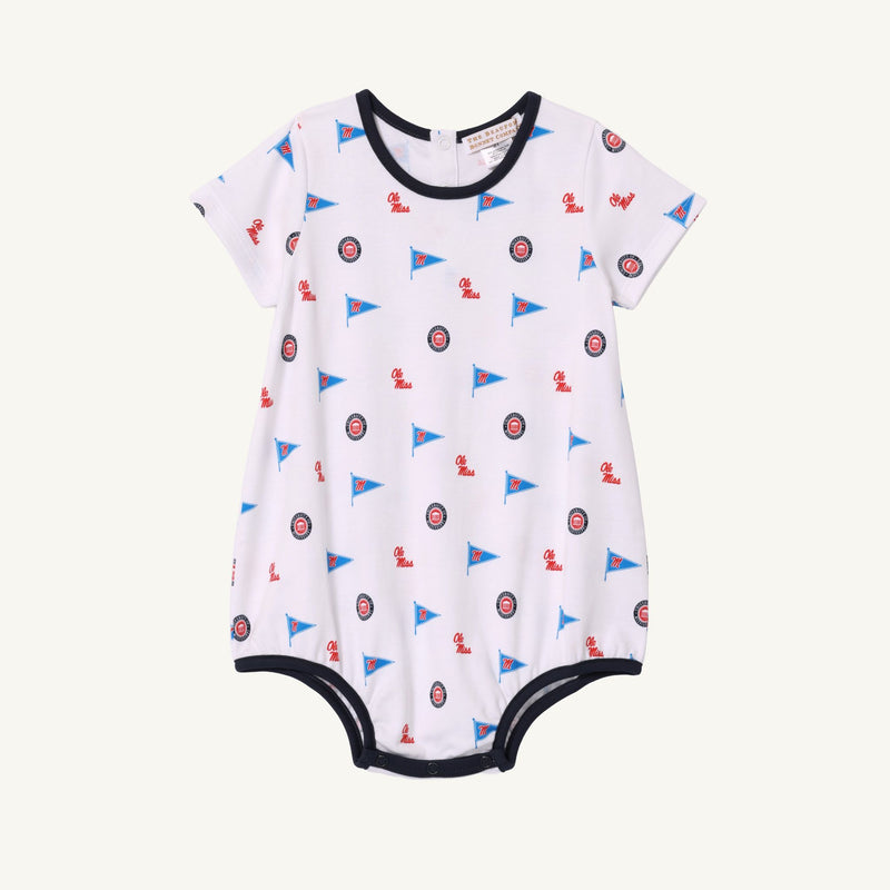 Ole Miss Short Sleeve Patton Play Bubble - Gawsh Almighty with Nantucket Navy by The Beaufort Bonnet Company, crafted from soft Pima Cotton and adorned with small blue flags and circular red, white, and blue emblems. Finished with dark blue trim along the neck, sleeves, and leg openings—perfect for little Ole Miss fans.
