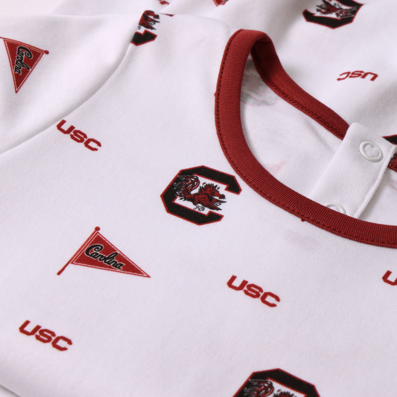 Here’s your rewritten sentence using the provided product data: Close-up of The Beaufort Bonnet Company’s USC Short Sleeve Patton Play Bubble - South Carolina Spirit with South Carolina Burgundy, a white short sleeve bubble garment detailed with maroon accents and printed logos—USC, a Gamecock mascot, and a triangular pennant marked “Carolina.” Crafted from soft Pima cotton, this shirt features a snap button near the collar for added convenience, perfectly capturing true South Carolina spirit.