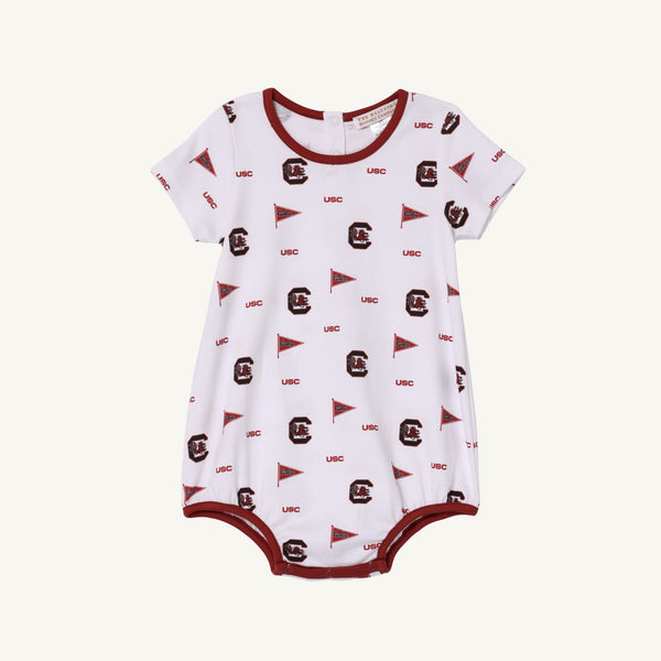 The Beaufort Bonnet Company’s USC Short Sleeve Patton Play Bubble - South Carolina Spirit with South Carolina Burgundy is a white baby romper featuring maroon trim, USC text, pennant flags, and stylized letter C logos in maroon. Crafted from soft Pima cotton, this short sleeve bubble includes snaps at the bottom for easy diaper changes—perfect for showing your South Carolina spirit.